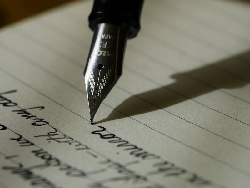 A fountain pen nib writing in ink on lined paper
