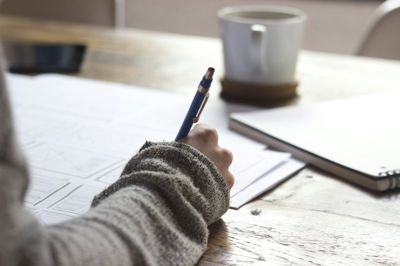 A student writing notes at a desk beside a cup of coffee