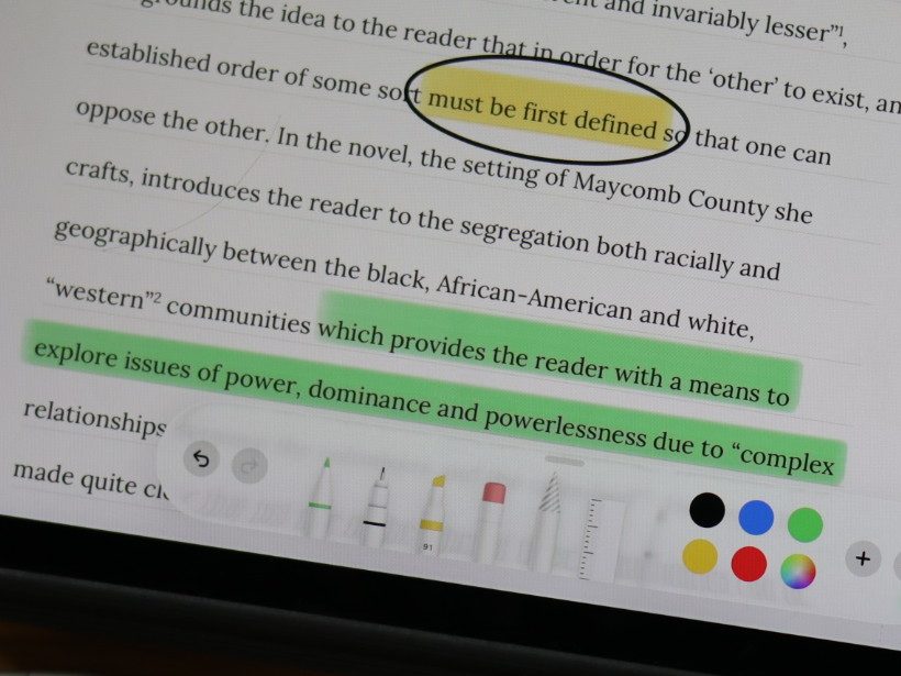 An essay on an iPad mid-marking, with a phrase circled in black and a passage highlighted in green.