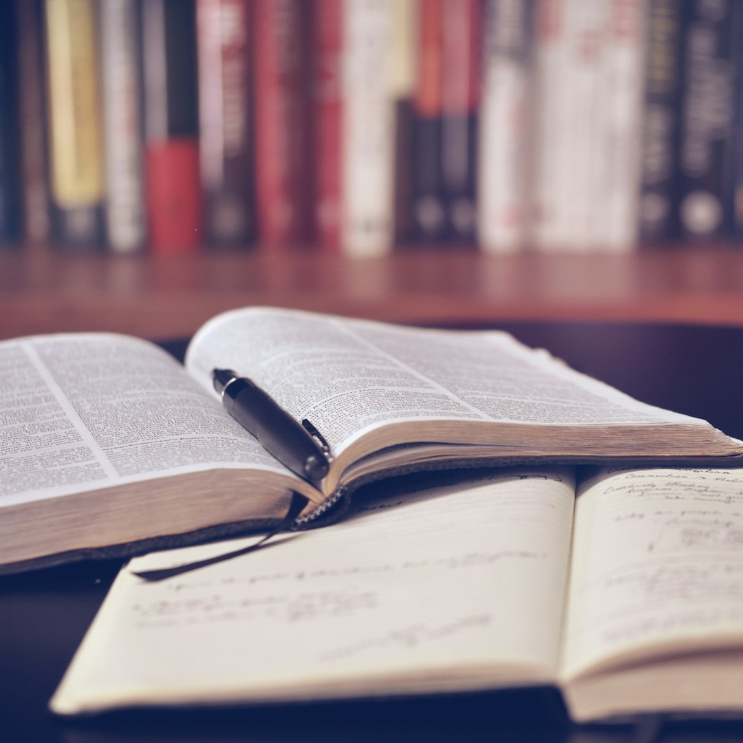 Open books and handwritten notes on a desk in front of a bookshelf